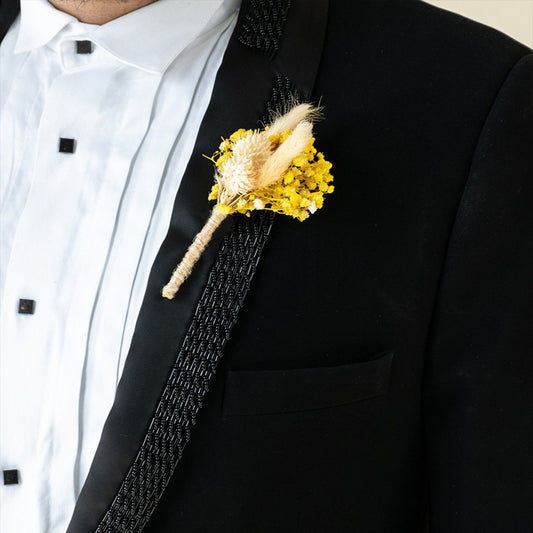 Artificial yellow rose boutonniere with greenery for wedding groom suit lapel floral accessory on white background.