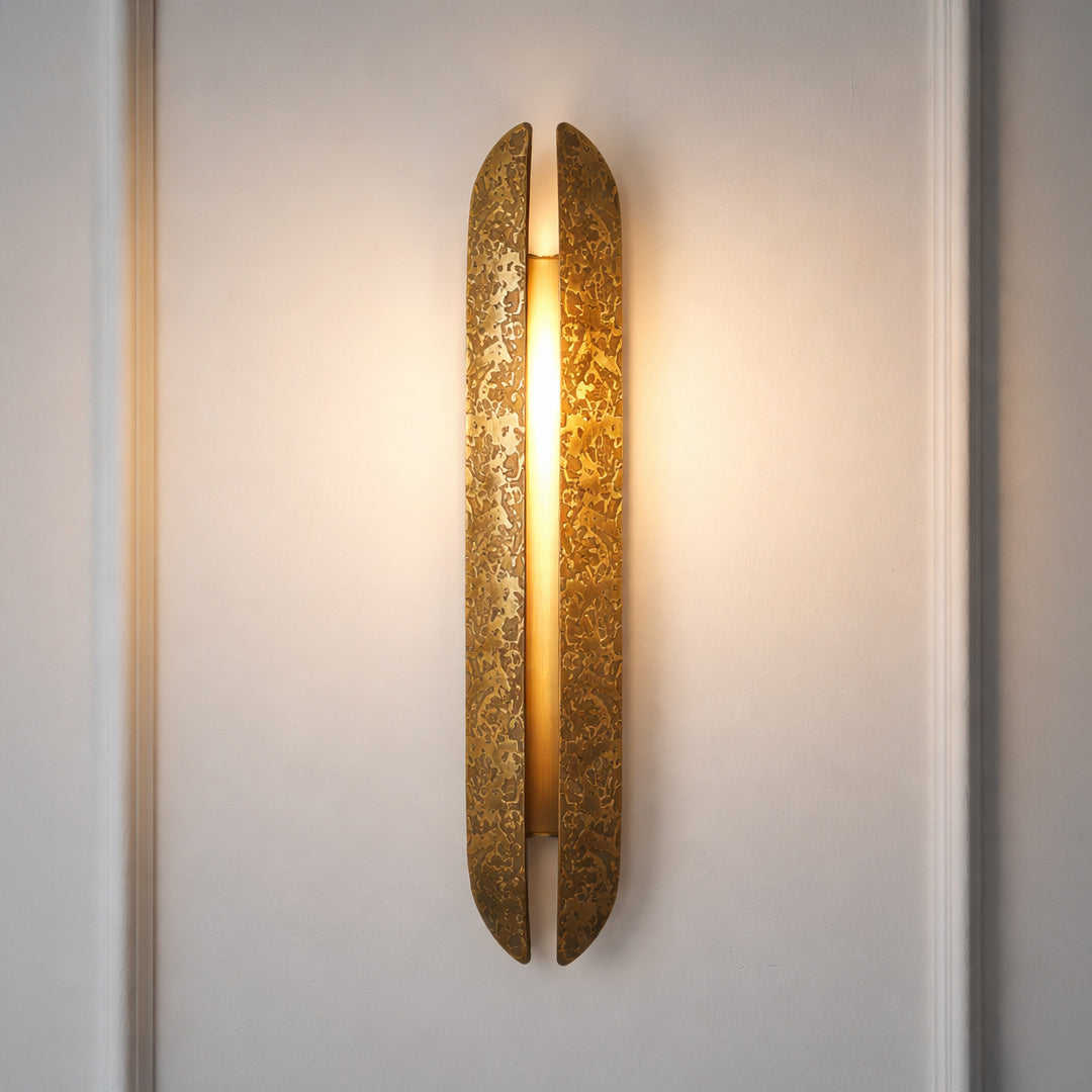 Contemporary gold wall sconce with glowing textured glass cylinder on neutral wall background ideal for elegant bedroom or hallway lighting.