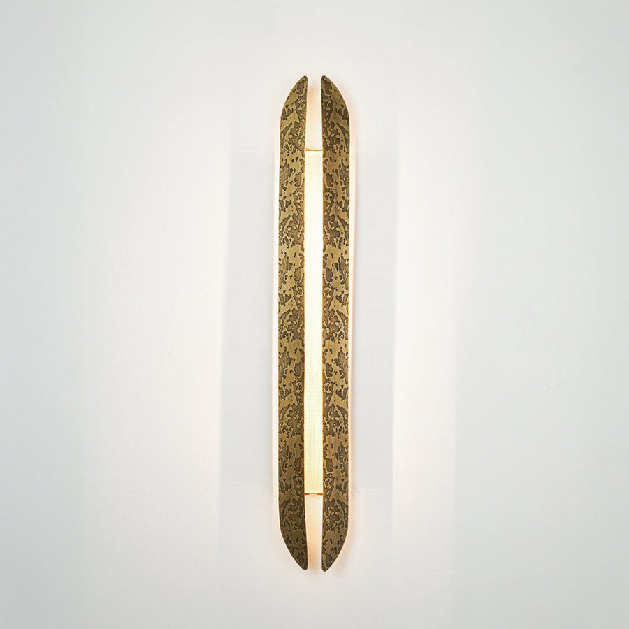 Gold wall light with elongated textured metal design mounted on neutral wall background ideal for modern luxury interior decor lighting.