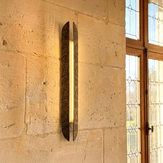 Modern gold wall light with vertical textured glass tube mounted on stone wall background creating warm ambient lighting in luxury interior setting.