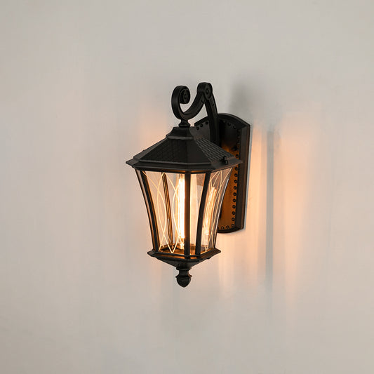 Black metal outdoor wall lantern on white background with clear tapered paneled glass shade for entryway patio decor.