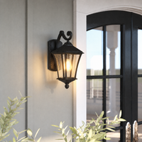 Rustic black iron curved arm glass wall lantern fixture on white siding next to arched window for outdoor porch lighting.