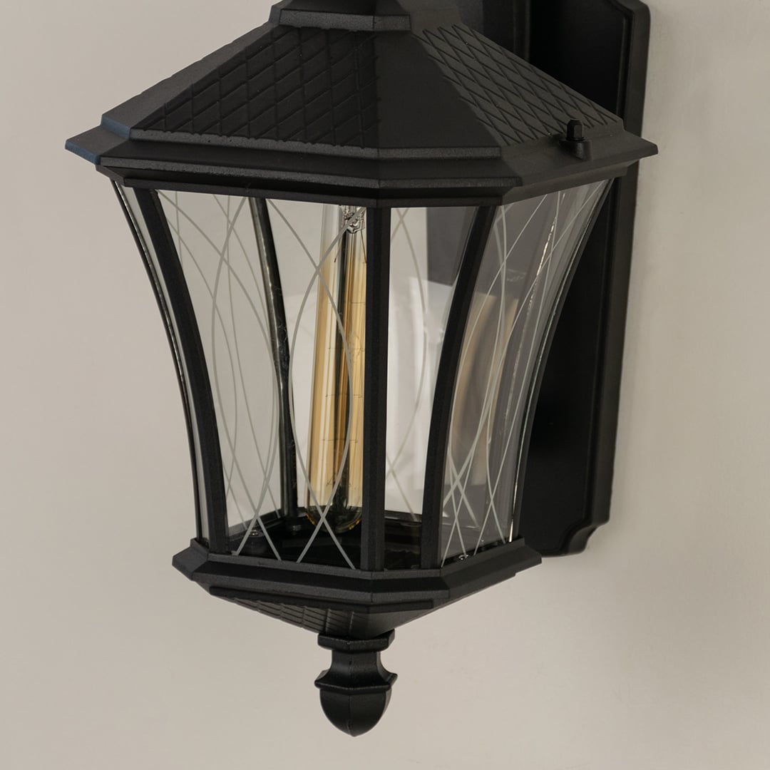 A closeup of the outdoor lantern showing the patterned clear glass panels warm glowing bulb and refined black frame for elegant exterior lighting presentation.