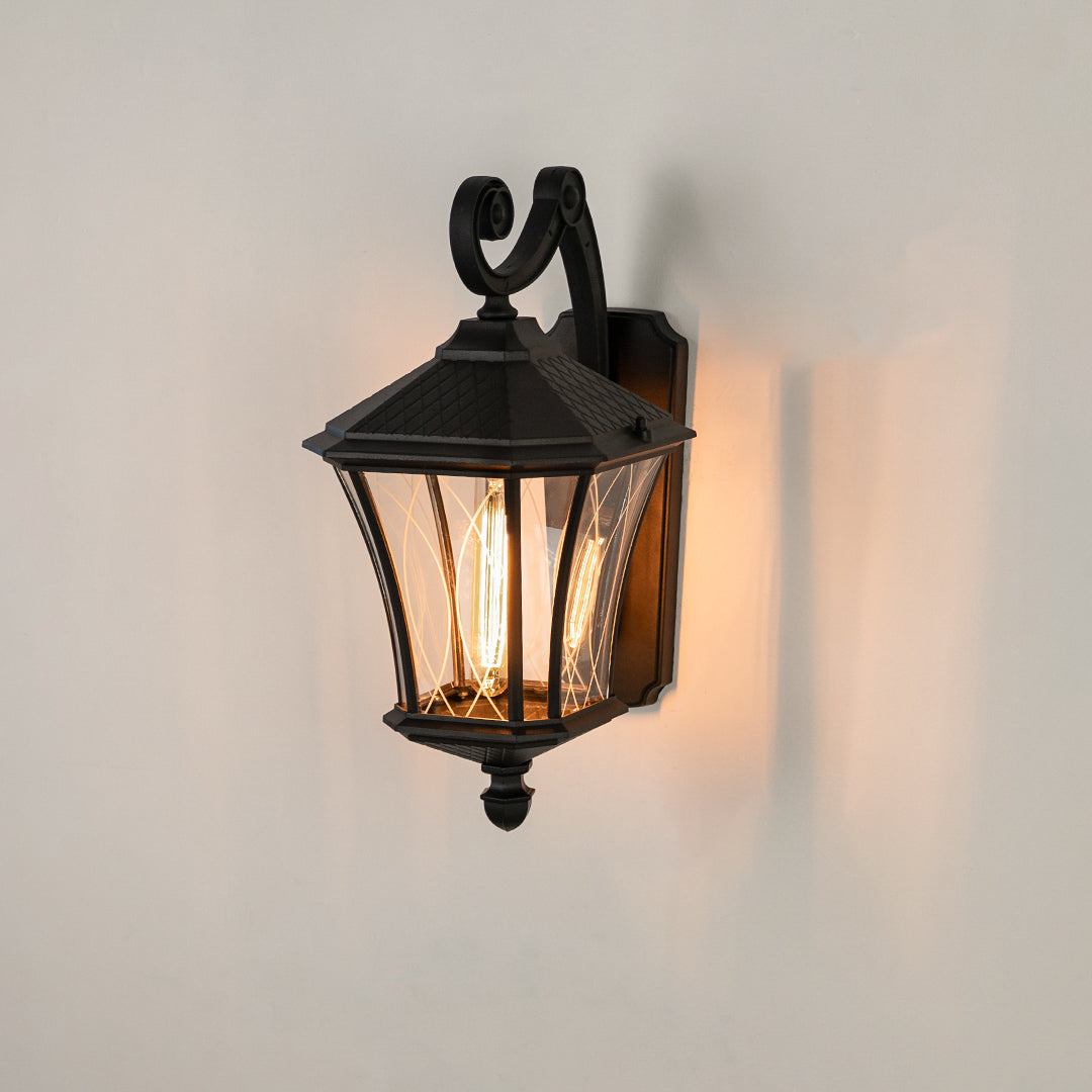 Black metal outdoor wall lantern on white background with a clear paneled glass shade for traditional patio decor.