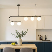 Black metal linear pendant light with white glass globes styled above dining table creating modern ambient ceiling lighting.