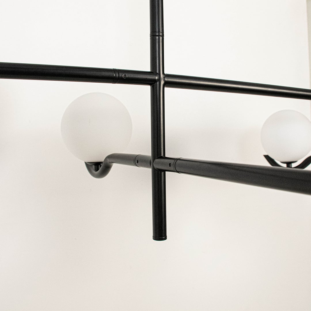 Closeup of black metal chandelier showing curved arms and matte white globes for stylish modern interior lighting.
