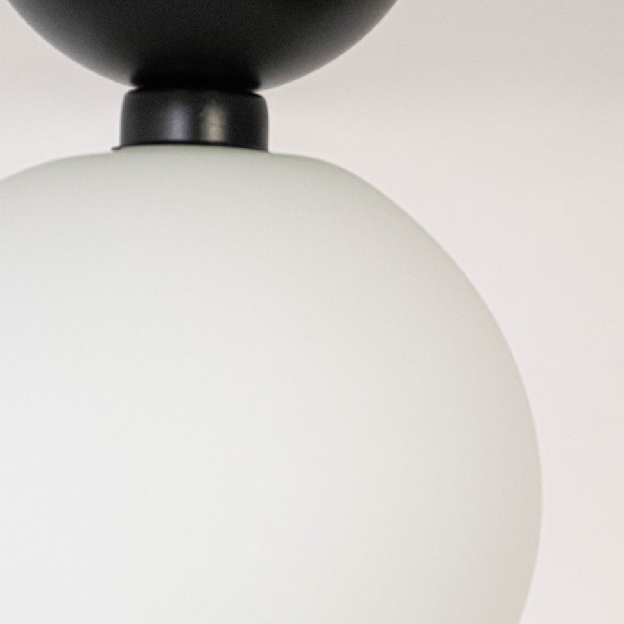 Closeup of ceiling light with black finish base and frosted glass globe shade for modern home lighting decor.