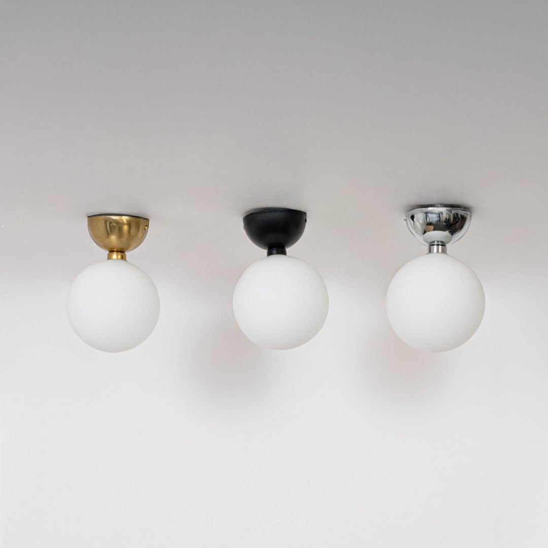 Collection of ceiling lights in black gold and chrome finish with frosted glass globe shades shown off on background.