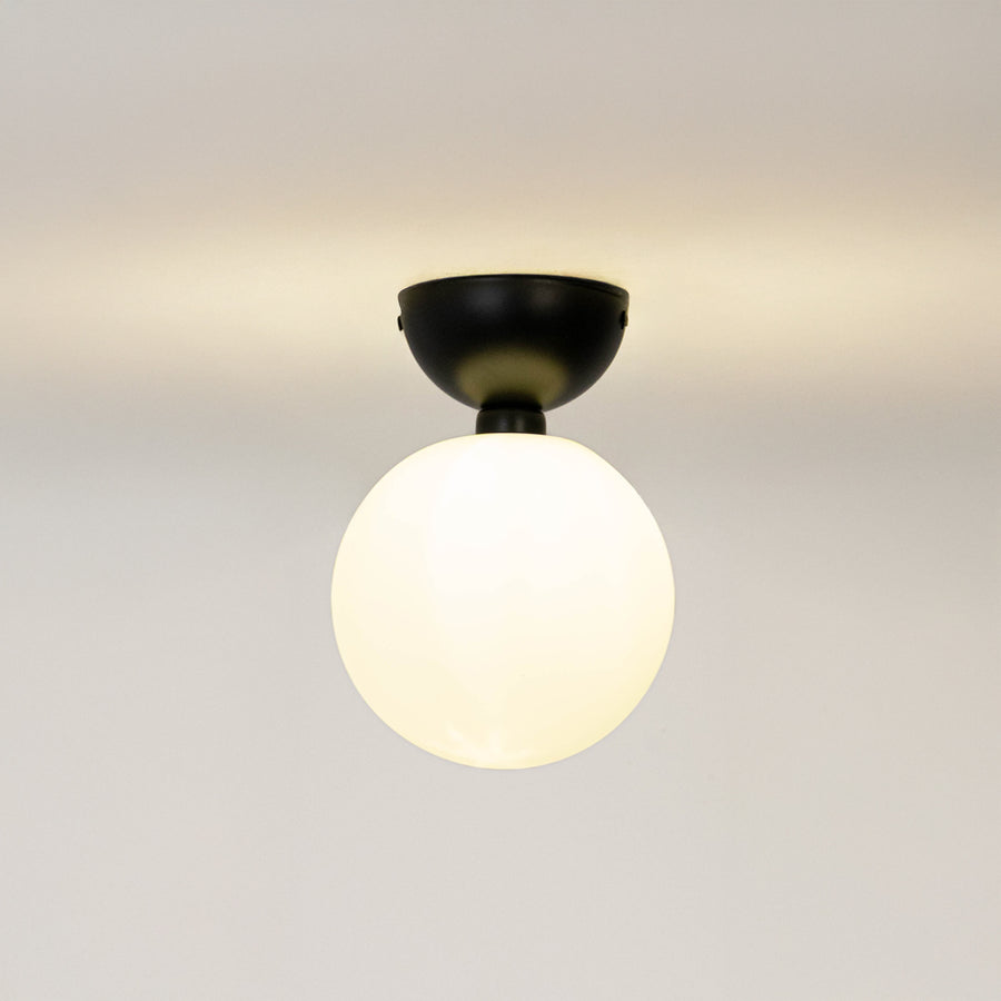 Modern black metal ceiling light with frosted white glass globe for contemporary bedroom and elegant decor styling spaces.