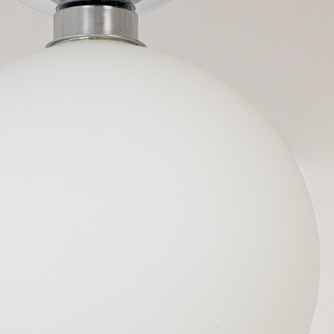 Closeup of ceiling light with chrome finish base and frosted glass globe shade for stylish modern home lighting.