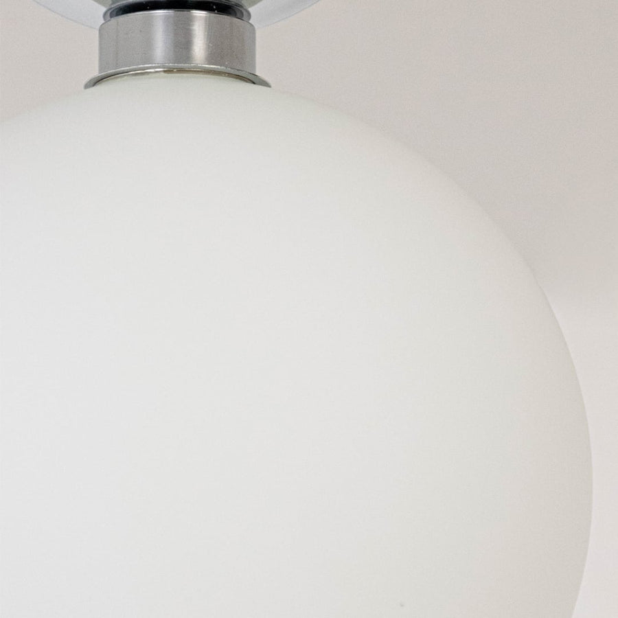 Closeup of ceiling light with chrome finish base and frosted glass globe shade for stylish modern home lighting.