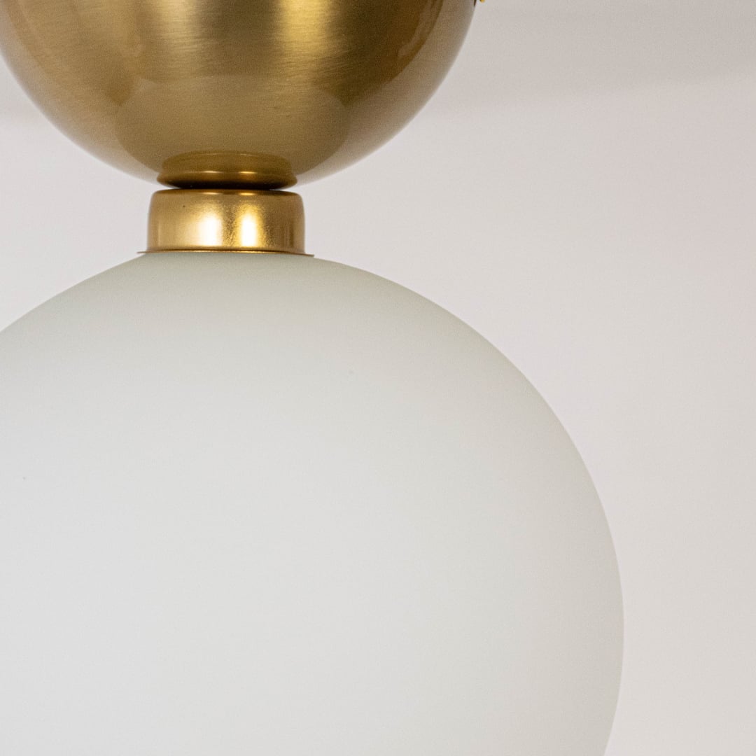 Closeup of ceiling light with brushed gold base and frosted glass globe shade for modern home lighting decor.