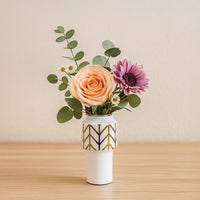 A modern white vase with gold geometric accents displayed on a clean surface adding a stylish decorative touch to a bright contemporary room.