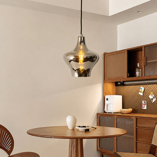 A modern pendant light with a reflective silver metallic dome-shaped shade hangs over a round wooden dining table in a warm, contemporary dining room setting.