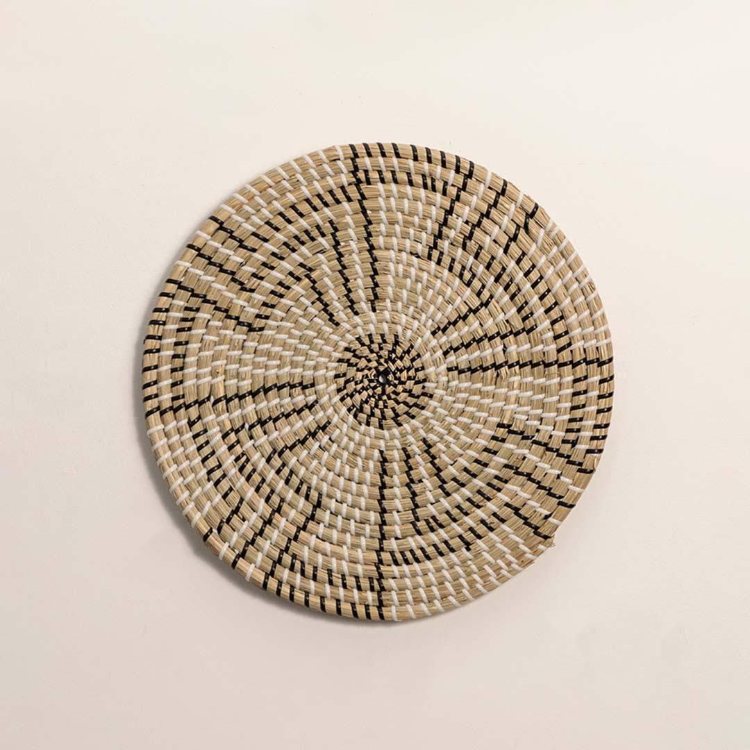 Round handcrafted black and natural seagrass wall basket with geometric stepped zigzag pattern on white background image.