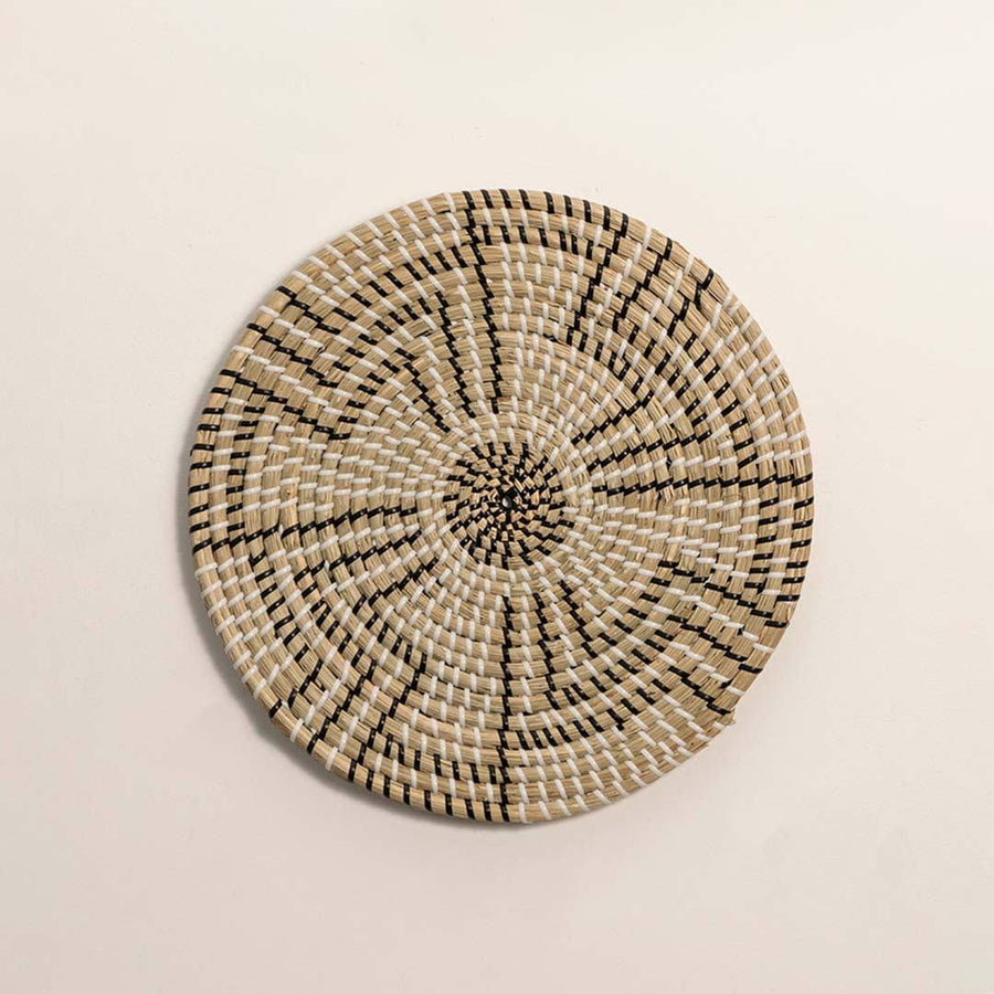 Round handcrafted black and natural seagrass wall basket with geometric stepped zigzag pattern on white background image.