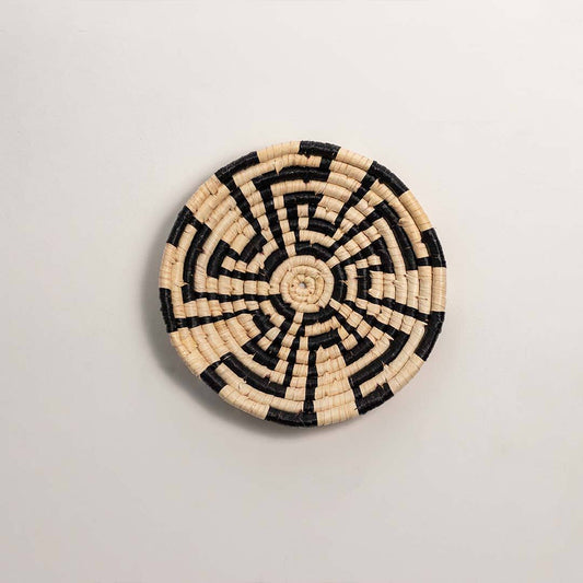 Round handcrafted black and cream seagrass wall basket with swirling abstract maze pattern on white background image.
