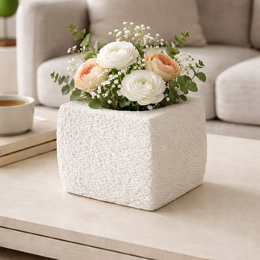 White textured polyresin square vase with floral arrangement placed on coffee table adding soft elegance to living room decor.