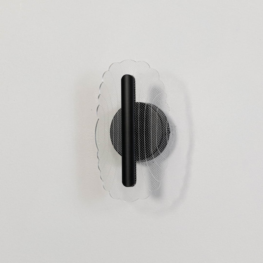Black metal wall light with clear acrylic patterned shade shown on a white background with lights off.