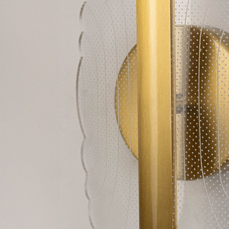 Closeup of gold metal wall light with clear acrylic patterned shade highlighting detailed texture and modern finish.