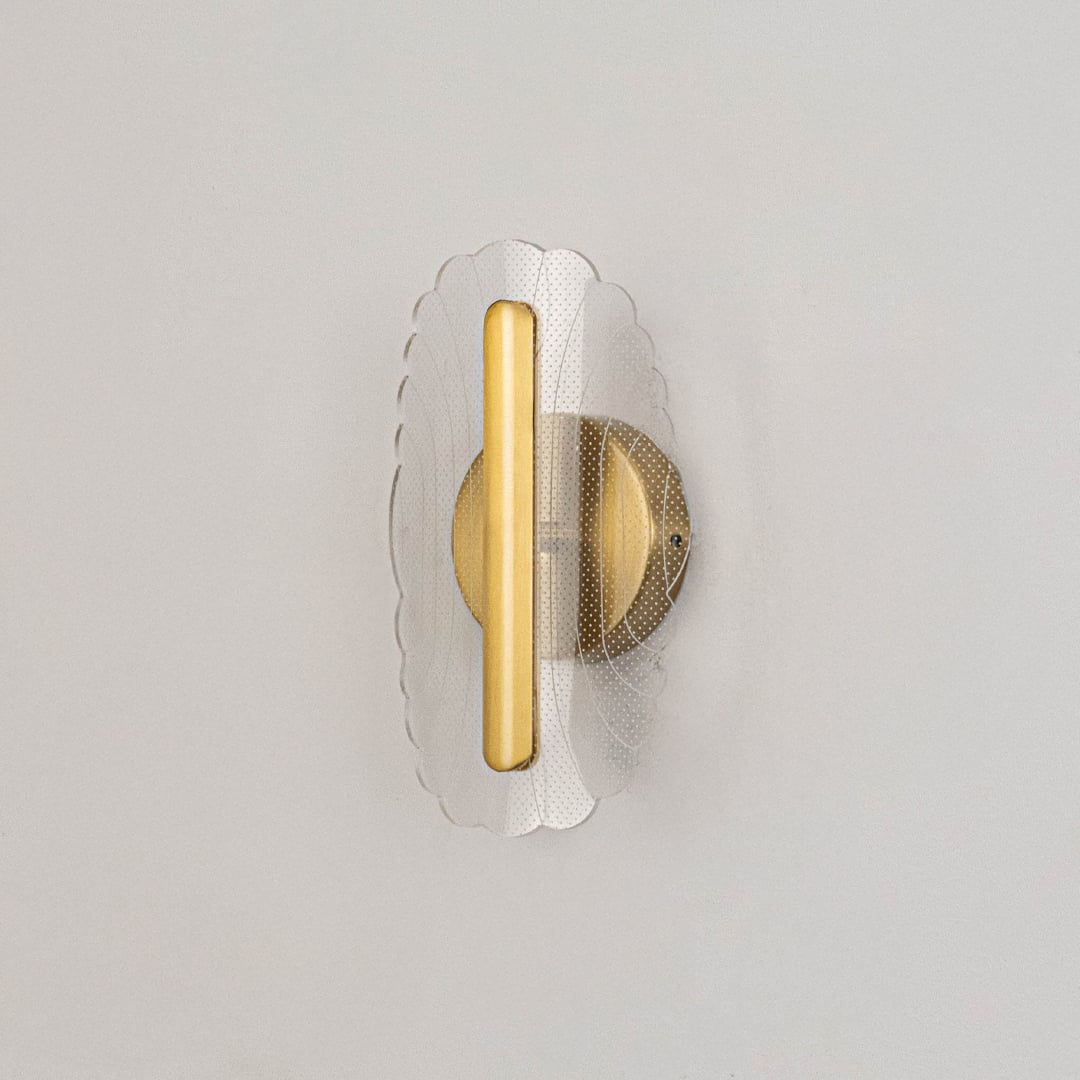Gold metal wall light with clear acrylic patterned shade shown on a white background with lights off.