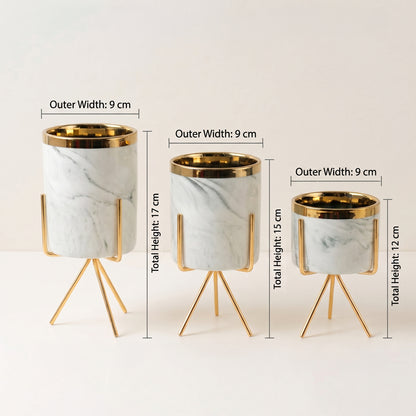 Three marble planters with gold metal rims and tripod stands, shown in different sizes with dimension labels for outer width and total height on a light neutral background.