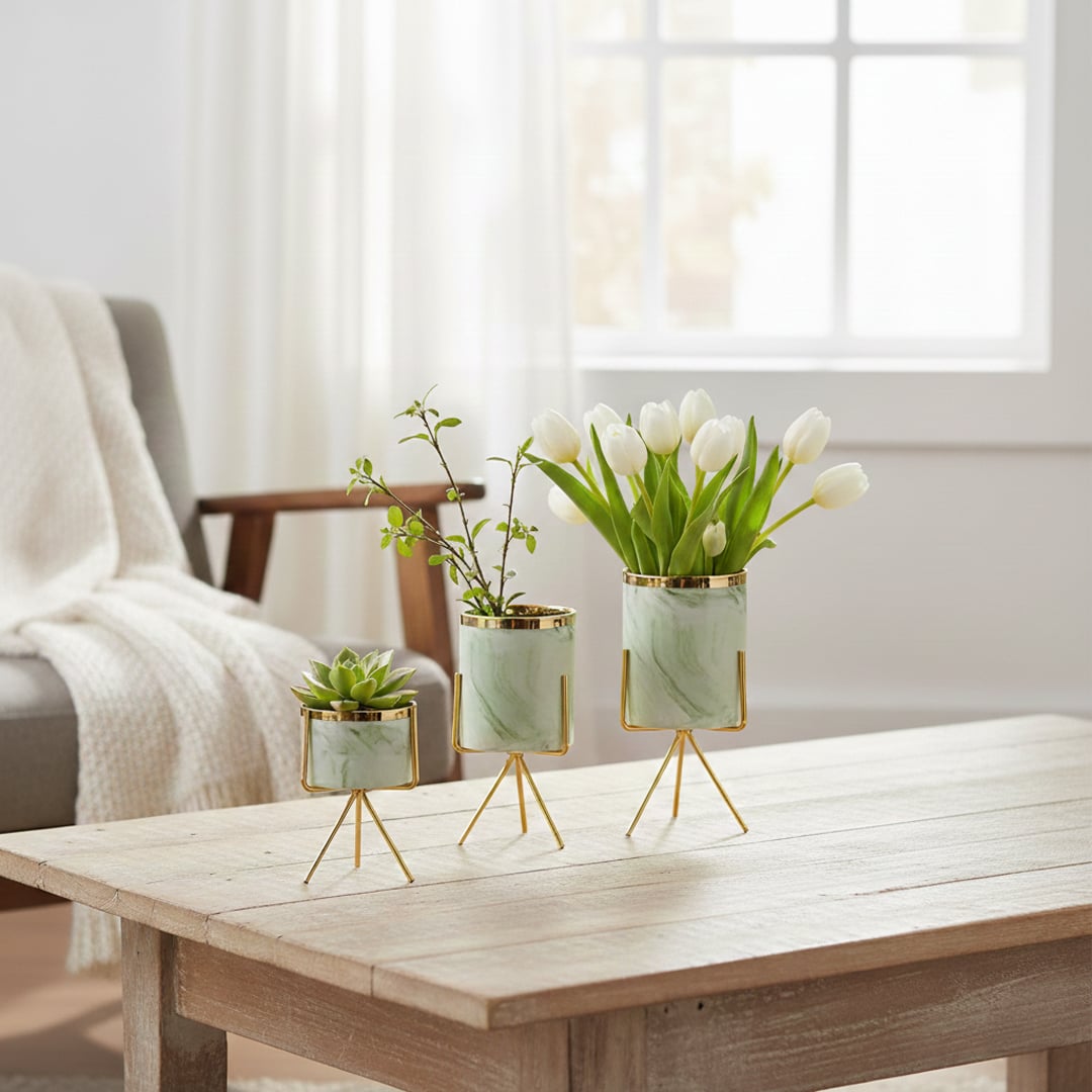 Lifestyle image of a trio of mint green planters on gold tripod stands styled with white tulips on a wood coffee table.