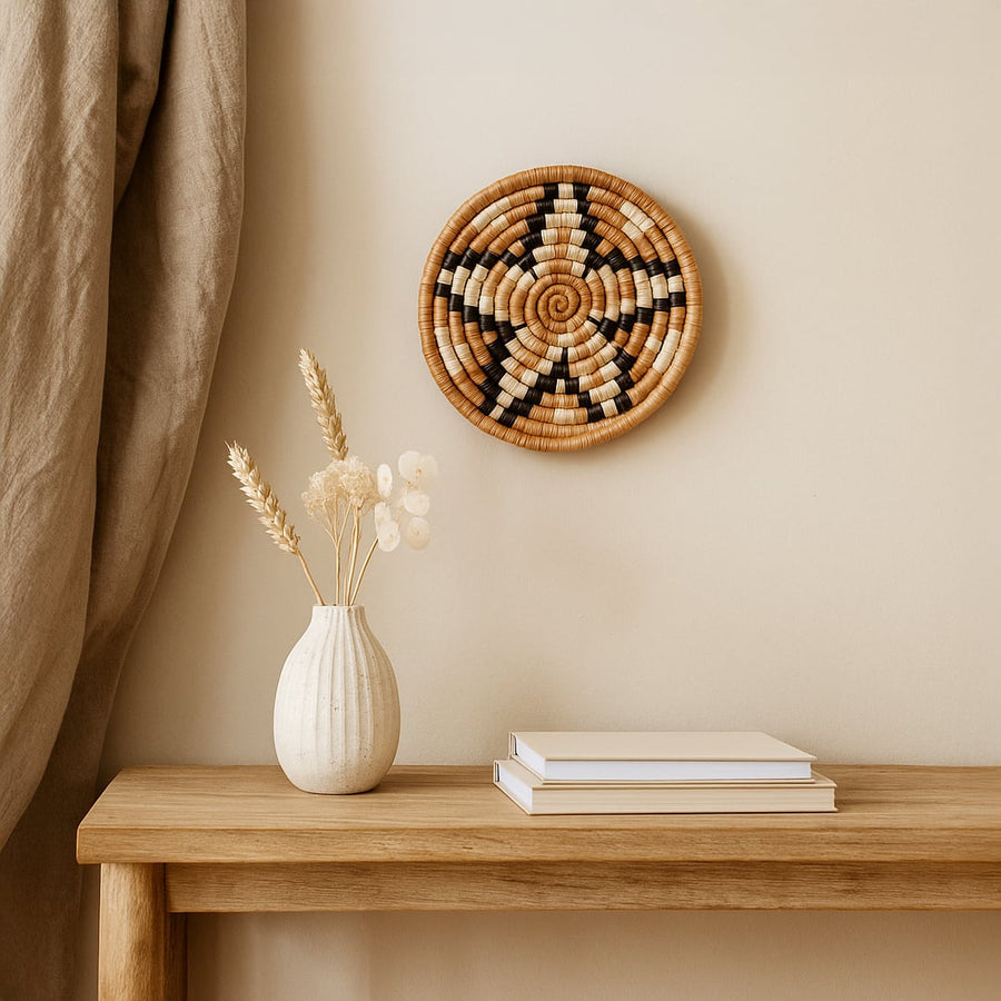 Woven round wall basket styled above wooden console with ceramic vase and books creating warm natural living room Decor focus.