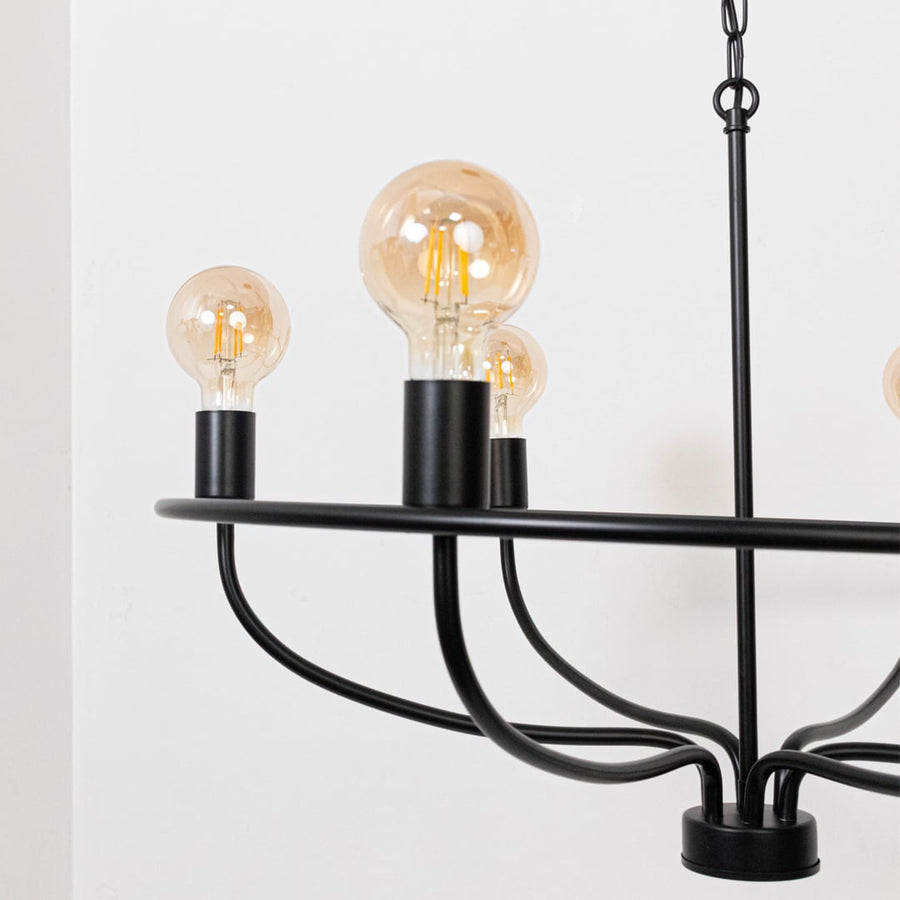 Detailed closeup of amber Edison globe bulb with black metal cylindrical socket on contemporary industrial wagon wheel chandelier.