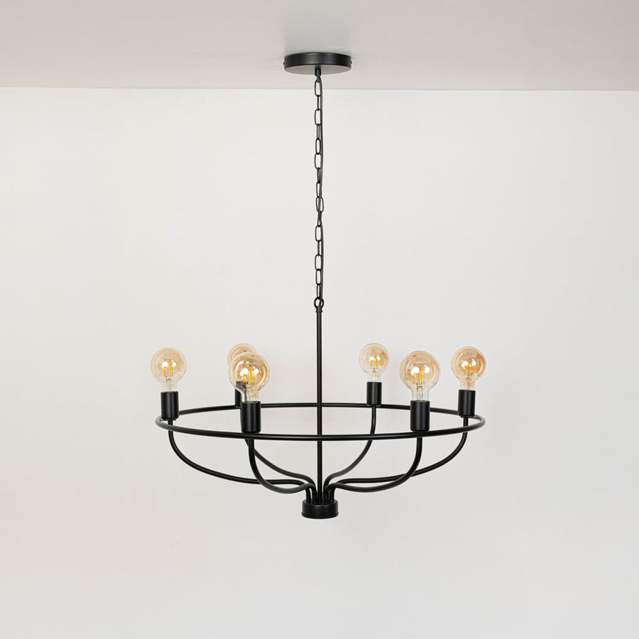 Contemporary black metal circular cage chandelier with chain and Edison bulb sockets turned off on clean white background.