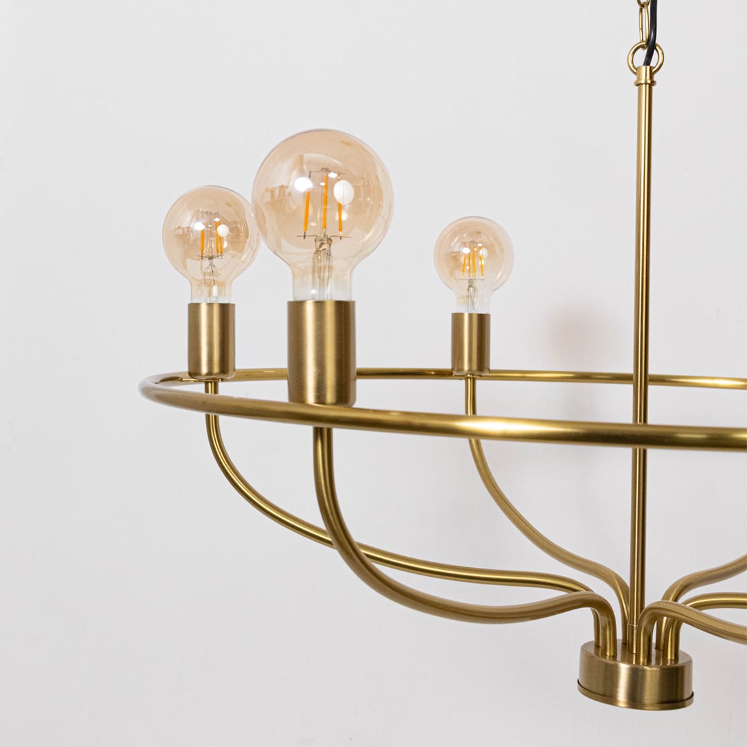 Detailed closeup of amber Edison globe bulb with brass gold cylindrical socket on contemporary vintage wagon wheel chandelier.