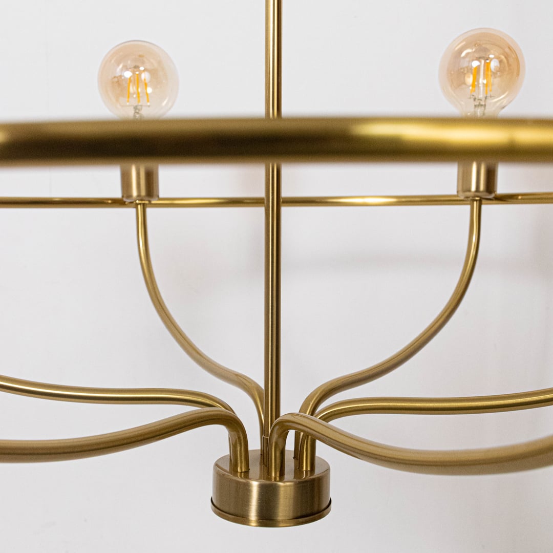 Closeup view of brass gold metal curved arms and cylindrical sockets with exposed Edison bulb on elegant chandelier frame.