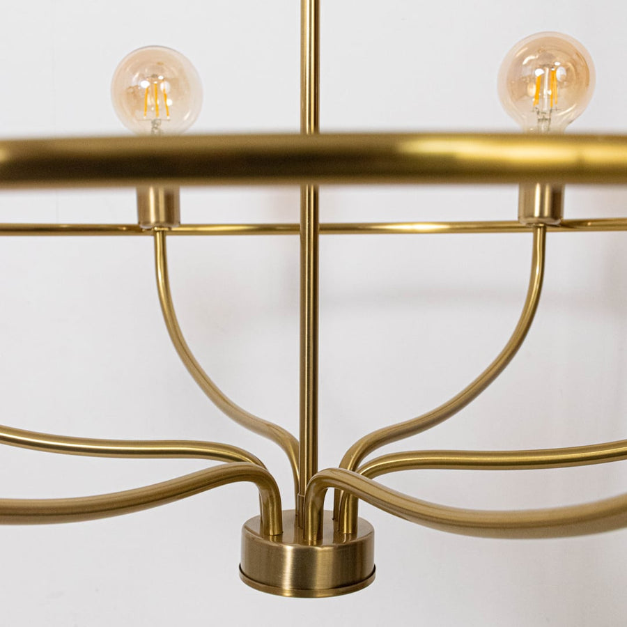 Closeup view of brass gold metal curved arms and cylindrical sockets with exposed Edison bulb on elegant chandelier frame.