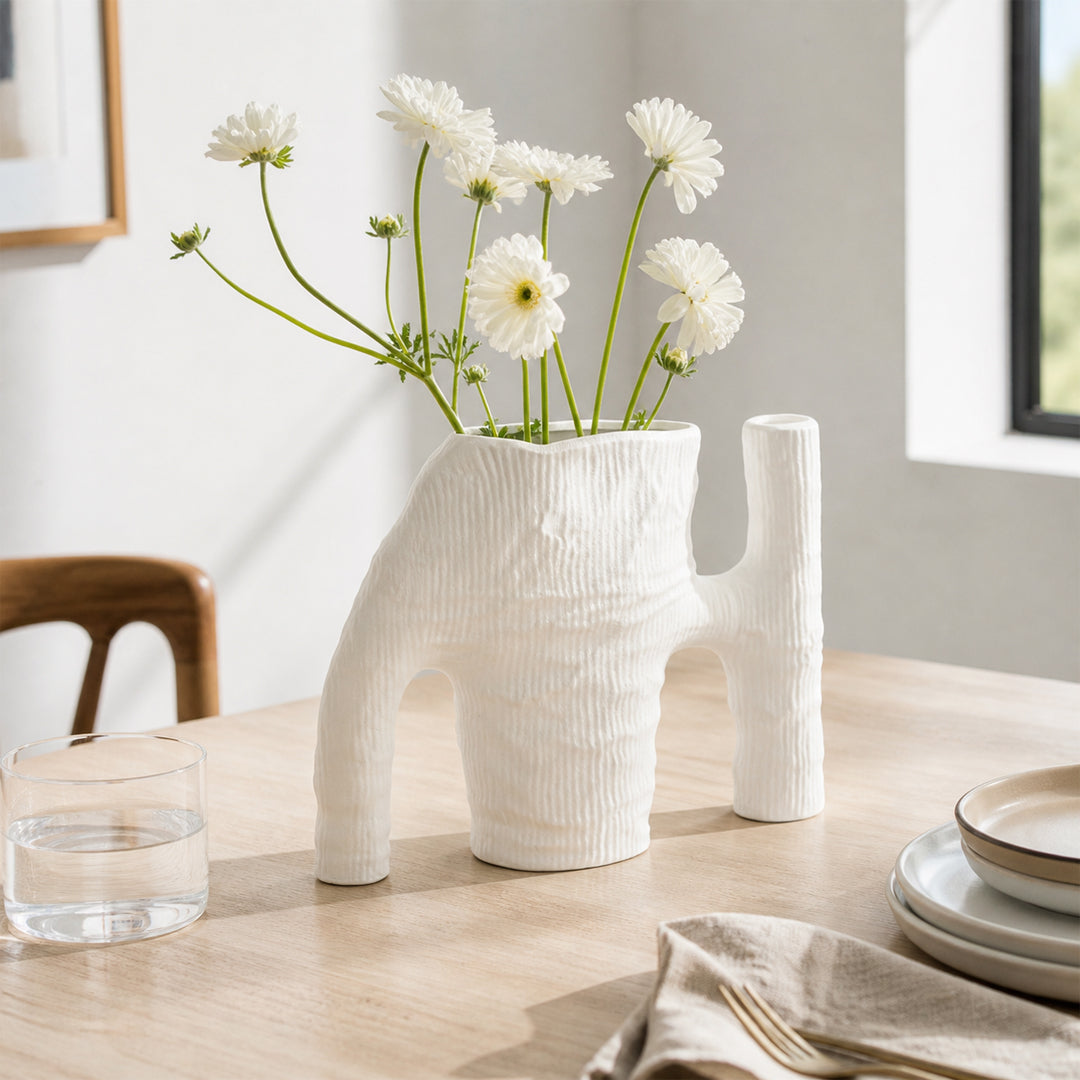White textured ceramic flower vase with fresh blooms placed on dining table for elegant modern home decor.