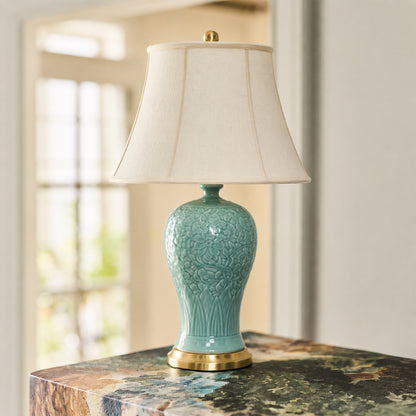 Turquoise ceramic table lamp with fabric shade placed on a wooden table creating warm traditional ambient lighting.