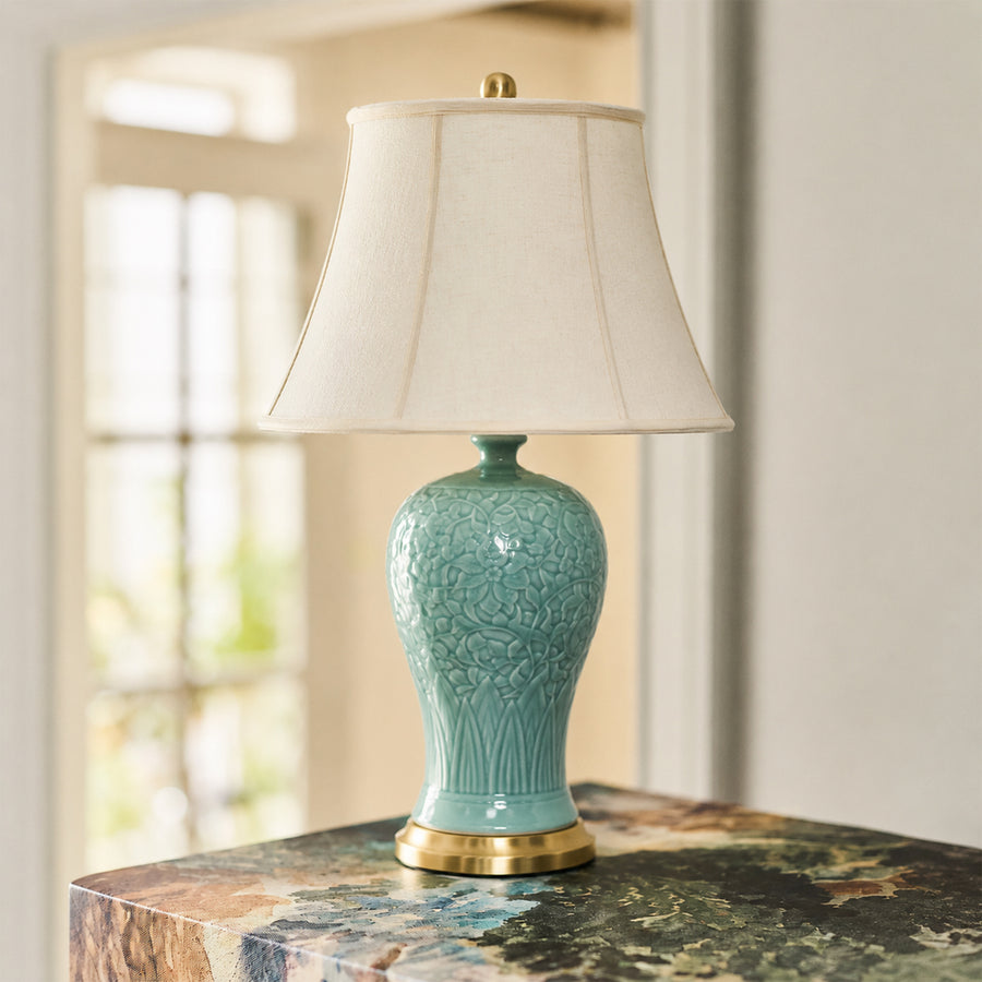 Turquoise ceramic table lamp with fabric shade placed on a wooden table creating warm traditional ambient lighting.