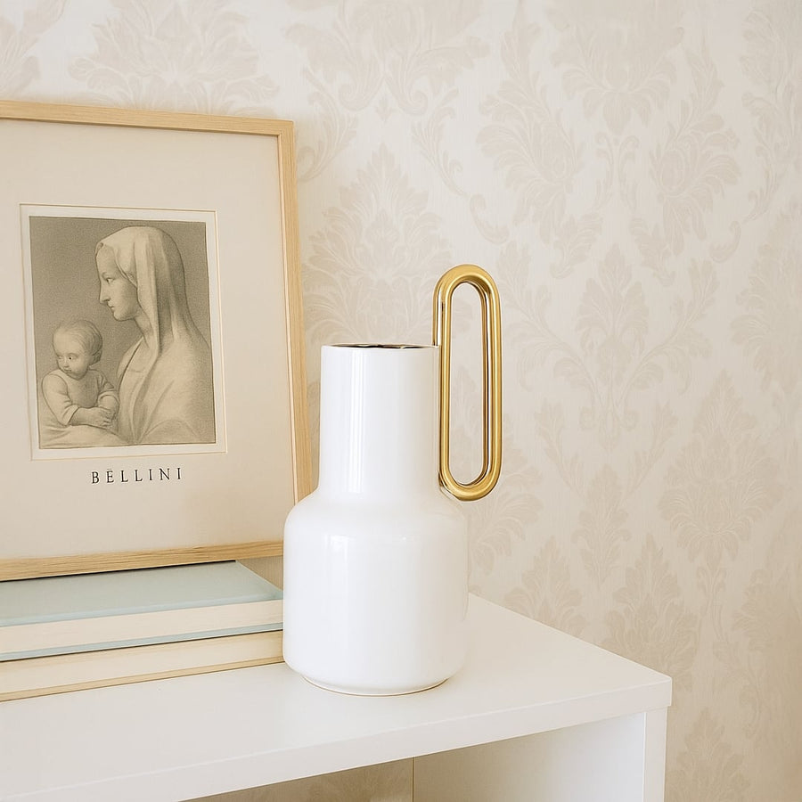 White ceramic vase with a gold handle styled in a modern interior perfect for consoles shelves and elegant contemporary home decor accents.