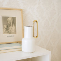 White ceramic vase with a gold handle styled in a modern interior perfect for consoles shelves and elegant contemporary home decor accents.