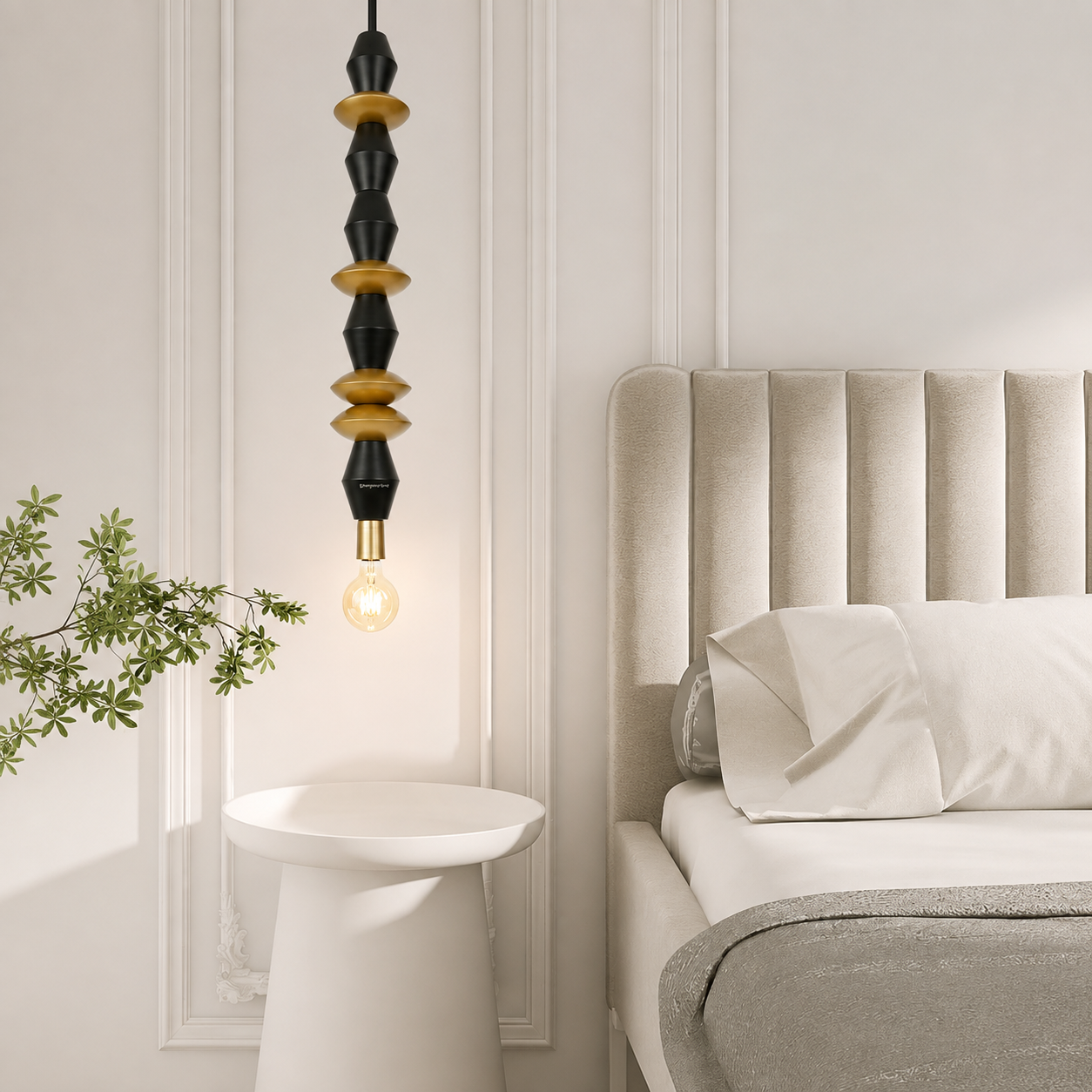 A modern pendant light with a black and gold beaded design hanging above a white side table in a styled bedroom setting next to a bed with a beige headboard.