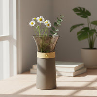 Modern grey vase with leather strap and gold button accent holding fresh flowers on sunlit wooden table decor display.