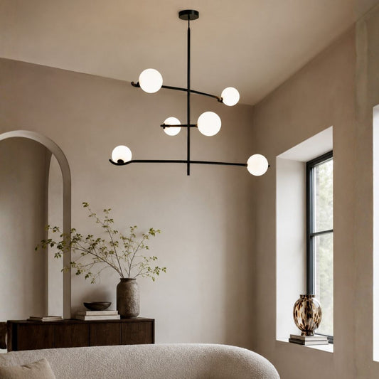 Modern multi-light linear chandelier with six matte white spherical globes on a black metal frame, hanging in a minimalist beige-toned room.