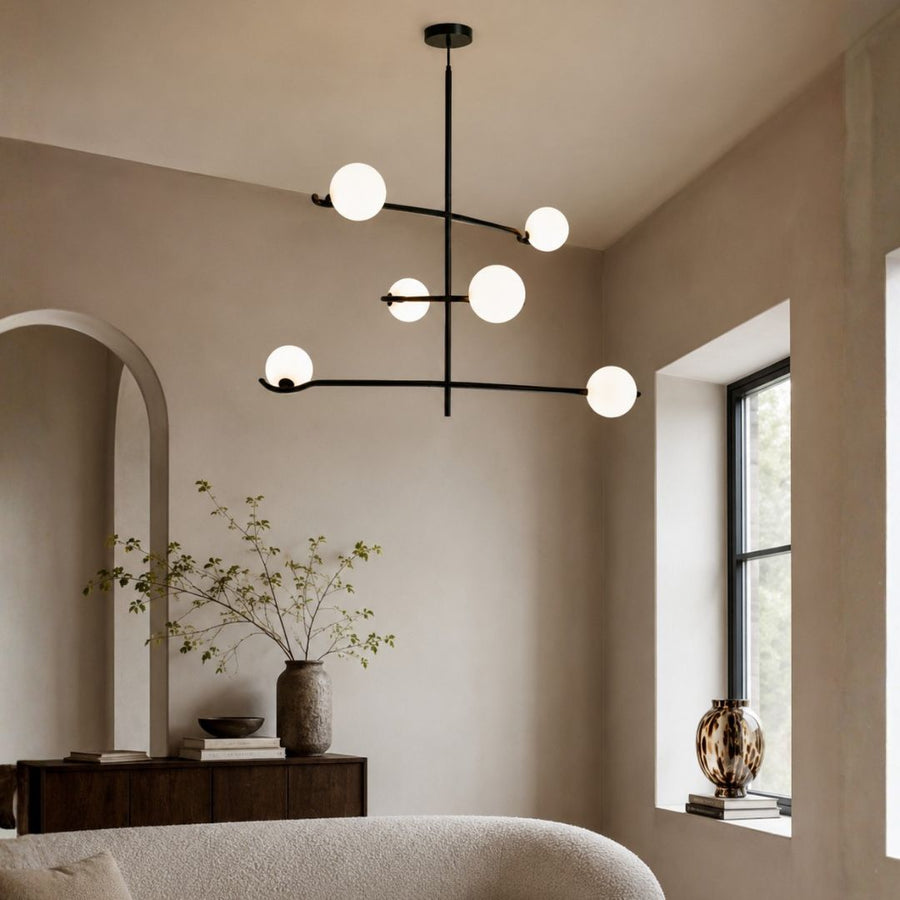 Modern multi-light linear chandelier with six matte white spherical globes on a black metal frame, hanging in a minimalist beige-toned room.