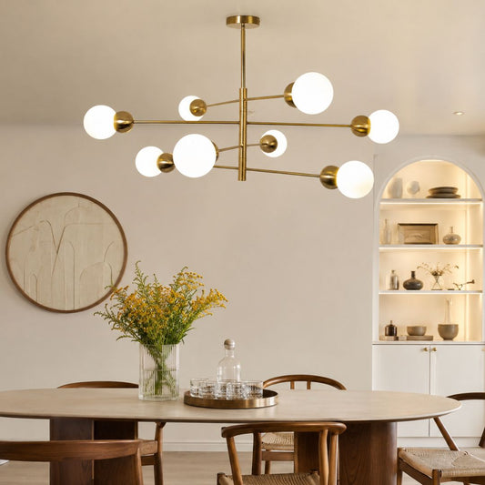 A modern multi-arm chandelier with a brushed brass/gold metal frame and multiple spherical white glass shades, hanging over a dining table in a styled dining room.