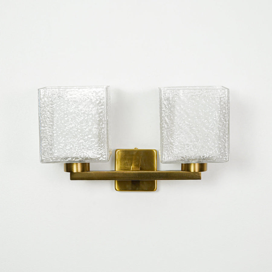 Contemporary gold wall light with ribbed glass shades mounted on clean white wall background ideal for modern interior lighting setup.

