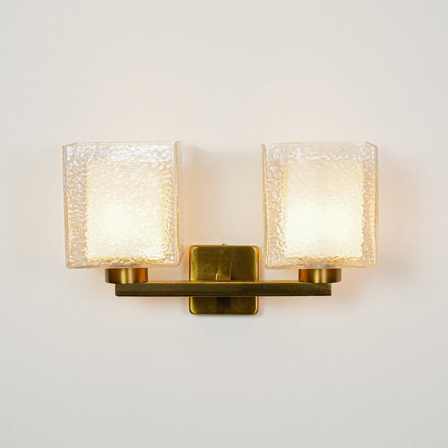 Elegant gold wall sconce with double textured glass shades on neutral wall background perfect for luxury bedroom or living room decor lighting.