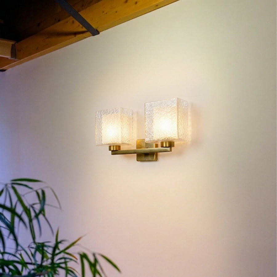 Modern gold wall light with dual frosted glass shades mounted on neutral wall background creating warm ambient lighting for contemporary interiors.