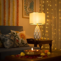 Gold ceramic table lamp with white shade glowing beside sofa for modern living room and bedroom interior lighting.