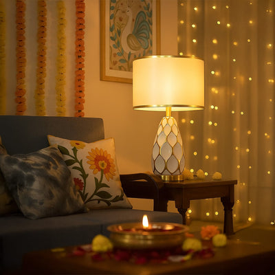 Gold ceramic table lamp with white shade glowing beside sofa for modern living room and bedroom interior lighting.