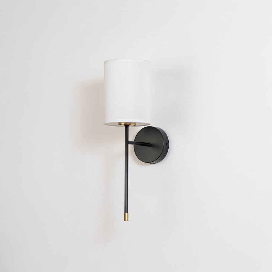 Modern white drum shade wall light fixture with black metal frame and brass accents turned off on clean white background.