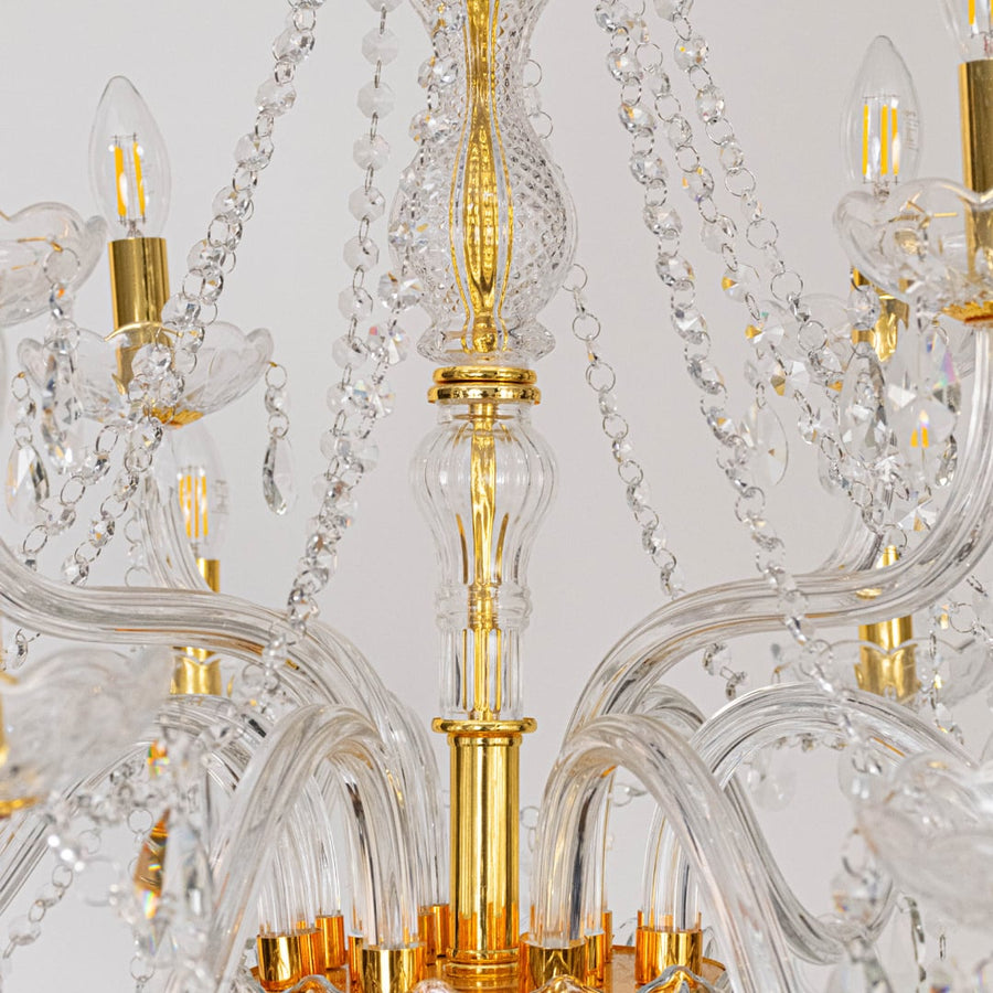 Closeup of chandelier showing gold detailing with crystal glass arms and hanging droplets for luxury design.